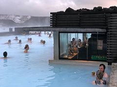02A People enjoy the blue hot water and the swim up bar with the Svartsengi geothermal power station in the background which supplies the hot water Blue Lagoon geothermal spa Iceland