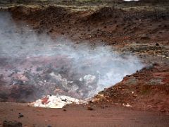 10C Hot steam fumarole surrounded by red soil with a few white rocks at Gunnuhver geothermal area Reykjanes Peninsula Iceland