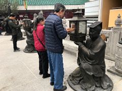 02C People lighting incense joss sticks from a lantern held by a kneeling statue Wong Tai Sin temple Hong Kong