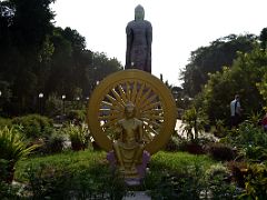 01C A Sitting Buddha In Front Of A Wheel With A Giant Buddha Statue Behind At The Thai Temple At Sarnath India