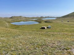 06B A small lake with Tulpar Lake beyond with a few nomad trailers dot the green fields on day hike from Ak-Sai Travel Lenin Peak Base Camp 3600m