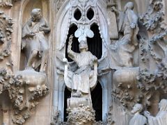 03C Jesus seated in a chair, his hands raised towards the sky. left is Saint John the Baptist, right is Saint Zachariah Faith portico Nativity facade Sagrada Familia Barcelona Spain